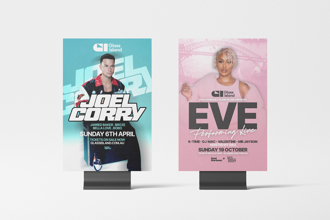 Teal Glass Island event poster featuring Joel Corry and a pink Eve poster, both displayed on black stands against a light backdrop with bold typography.