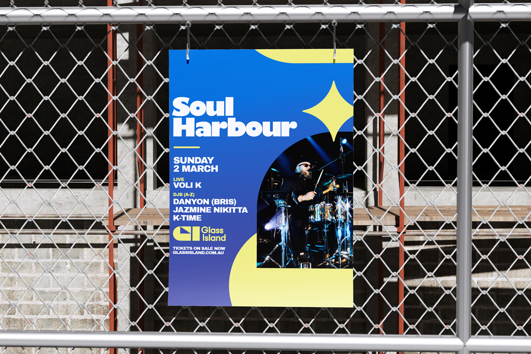 Blue and yellow Soul Harbour event poster featuring a drummer on a dark stage, mounted on a chain-link fence, with Glass Island branding and bold typography.
